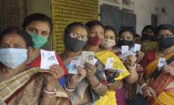 Women show their voter ID card, as they stand in a queue to
